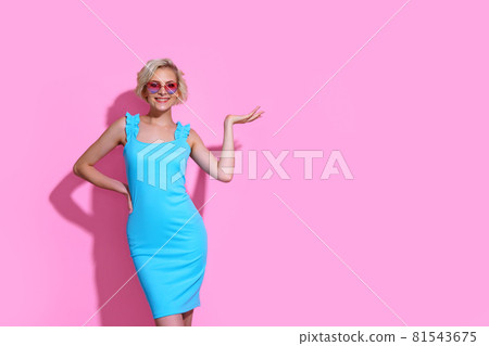 Portrait of beautiful blonde woman in blue dress with sunglasses posing on pink studio background Portrait of beautiful blonde woman in blue dress with sunglasses posing on pink studio background 81543675