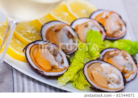 Tasty raw dog cockle, lemon and greens at plate and glass of wine 81544071