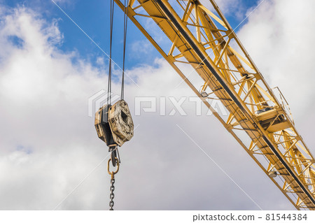 Overhead crane hoist industrial mechanism with hook and chain on a background of blue sky with clouds, close-up Overhead crane hoist industrial mechanism with hook and chain on a background of blue sky with clouds, close-up 81544384