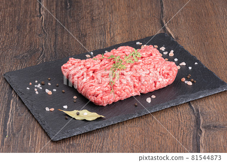 Ground beef with thyme and spices on a stone board over a wooden background. 81544873