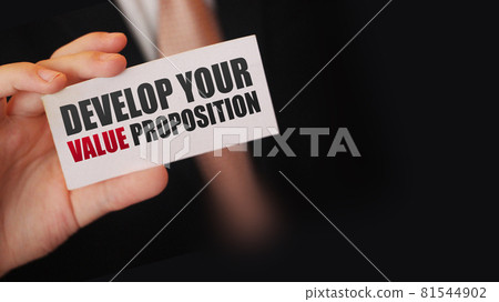 Businessman shows a card with text DEVELOP YOUR VALUE PROPOSITION. Management business achievements motivation concept Businessman shows a card with text DEVELOP YOUR VALUE PROPOSITION. Management business achievements motivation concept 81544902