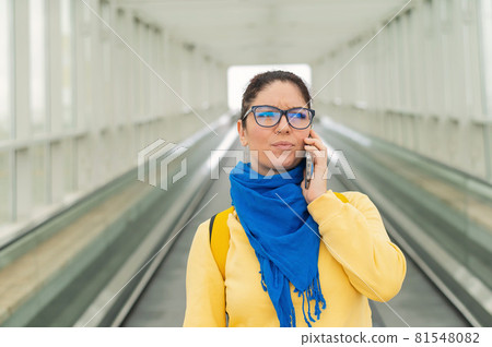 Caucasian woman stands on the escalator and is displeased talking on the mobile phone. 81548082