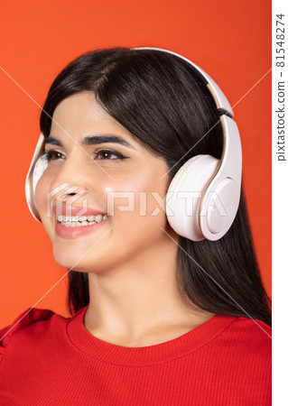 Close-up cropped portrait of of young beautiful girl in headphones isolated over orange background. 81548274