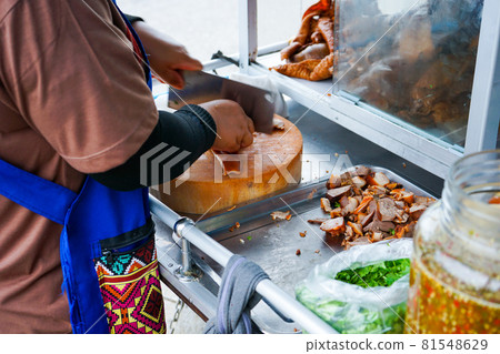 Delicious stewed ear pork at the street food. Motion blurred hand of seller chops the pork on cutting board. Delicious stewed ear pork at the street food. Motion blurred hand of seller chops the pork on cutting board. 81548629