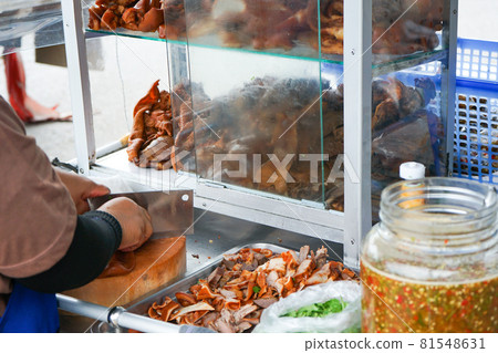 Delicious stewed ear pork at the street food. Motion blurred hand of seller chops the pork on cutting board. Delicious stewed ear pork at the street food. Motion blurred hand of seller chops the pork on cutting board. 81548631