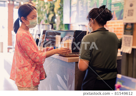 Asian Woman customer in protective mask receive drink from waiter on coffee bar counter. 81549612
