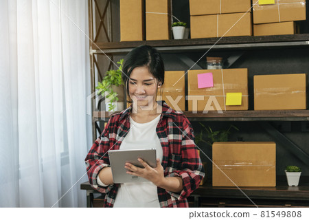 Asian woman startup small business at home office. Online seller entrepreneur young asian woman use tablet checking online order. Woman using tablet check stock goods supply delivery package shipping 81549808