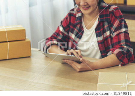 Asian woman startup small business at home office. Online seller entrepreneur young asian woman use tablet checking online order. Woman using tablet check stock goods supply delivery package shipping 81549811