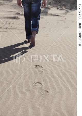 Legs of young guy walking barefoot on the sand leaving footprints in his wake Legs of young guy walking barefoot on the sand leaving footprints in his wake 81550725