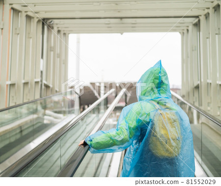 A woman in a raincoat rises on an escalator. Girl in protective clothing from the rain. Back view. A woman in a raincoat rises on an escalator. Girl in protective clothing from the rain. Back view. 81552029