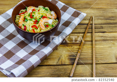 Bowl of instant Chinese noodles with shrimps, green onion and red hot chilli peppers on wooden table 81552540