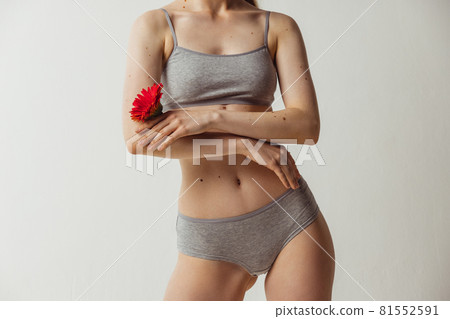 Cropped shot of young attractive woman holding flower as symbol of tenderness isolated over gray studio background. Natural beauty, authenticity concept. Cropped shot of young attractive woman holding flower as symbol of tenderness isolated over gray studio background. Natural beauty, authenticity concept. 81552591