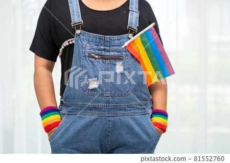 Asian lady wearing blue jean jacket or denim shirt and holding rainbow color flag, symbol of LGBT pride month celebrate annual in June social of gay, lesbian, bisexual, transgender, human rights. Asian lady wearing blue jean jacket or denim shirt and holding rainbow color flag, symbol of LGBT pride month celebrate annual in June social of gay, lesbian, bisexual, transgender, human rights. 81552760