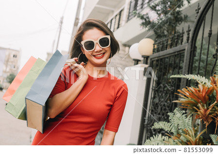 Happy asian woman with bags after shopping center in front of house. Happy asian woman with bags after shopping center in front of house. 81553099