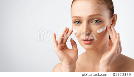 Young Woman Applying Moisturizer Cream On Cheeks Over Gray Background Young Woman Applying Moisturizer Cream On Cheeks Over Gray Background 81553379