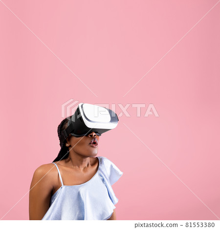 Cyberspace. Shocked African American woman wearing VR helmet, experiencing virtual reality on pink background 81553380