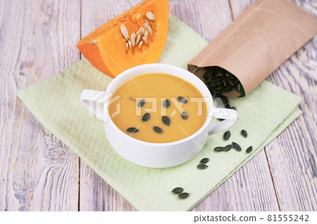 Close-up of a plate of pumpkin cream soup on a napkin napkin with scattered pumpkin seeds. Horizontal orientation Close-up of a plate of pumpkin cream soup on a napkin napkin with scattered pumpkin seeds. Horizontal orientation 81555242