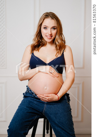 an attractive pregnant woman with a bare tummy sits on a chair. an attractive pregnant woman with a bare tummy sits on a chair. 81563370