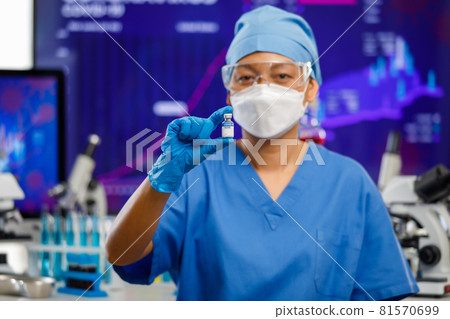 Female medical people wearing a hygiene face mask and protective glass staying in laboratory room, holding Covid-19 vaccine bottle with lab equipment in blur background 81570699