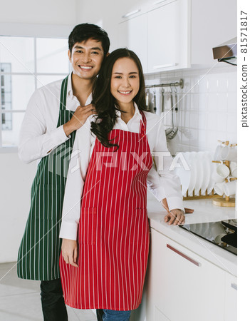 Young attractive Asian couple wearing green and red aprons smiling at camera. Concept for healthy and happy love and cooking 81571817