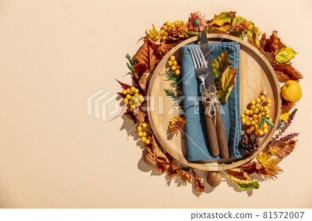 Autumn thanksgiving table place setting with cutlery, wooden plate and arrangement of fall leaves Autumn thanksgiving table place setting with cutlery, wooden plate and arrangement of fall leaves 81572007