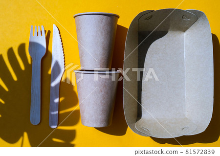 Wooden forks and paper cups with plates on color background. Eco friendly disposable tableware. Used in fast food, restaurants, takeaways, picnics. No plastic 81572839