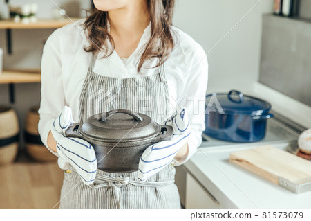 A woman in the kitchen wearing a mittens and holding a pot with both hands woman kitchen 81573079