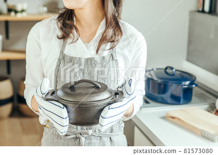 A woman in the kitchen wearing a mittens and holding a pot with both hands woman kitchen 81573080