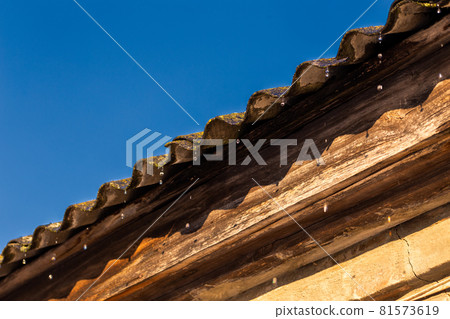 spring water drops flying from edge of an old barn roof 81573619