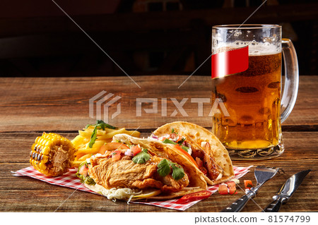 First corn tortilla with grilled chicken fillet, second with fish fillet, sauce and beer on wooden table 81574799