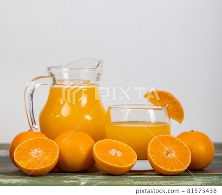 Fresh orange juice in clear jar and glass decorating with fresh orange on colourful wooden table. Studio picture concept for healthy diet. Studio picture Fresh orange juice in clear jar and glass decorating with fresh orange on colourful wooden table. Studio picture concept for healthy diet. Studio picture 81575438