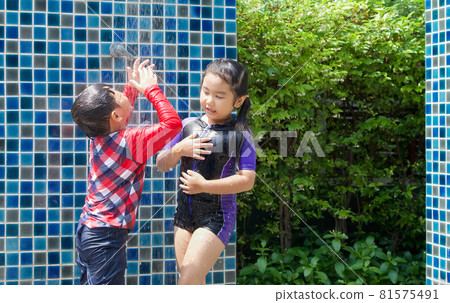 Asian kid wash salt water out of his face. The older sister shower her body after playing in the swimming pool. 81575491