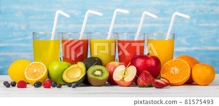Different fruits juice in glass, apple, orange and strawberry juice with straw, looking refreshing on colourful wood board in front of blue wall background. Picture decorating with fresh fruits 81575493