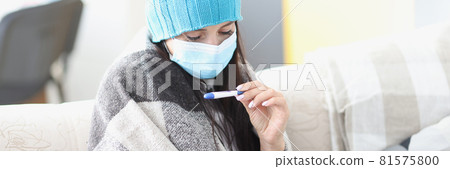 Woman in cap and protective medical mask looking at thermometer Woman in cap and protective medical mask looking at thermometer 81575800