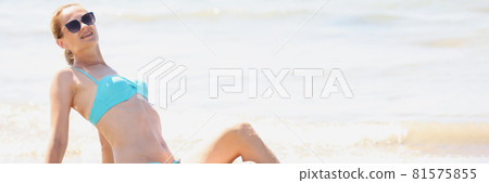 Young woman in sunglasses and swimsuit lying on beach 81575855