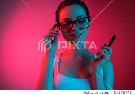 Cropped portrait of young beautiful girl in glasses on gradient pink red background 81576748