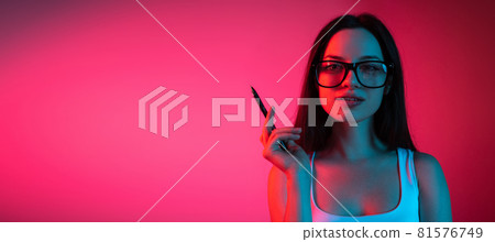 Cropped portrait of young beautiful girl in glasses on gradient pink red background 81576749