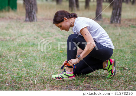 Young fitness woman fastens her participant chip before start of running race in the forest 81578250
