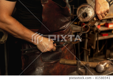 Close-up hands of male blacksmith forge an iron product in a blacksmith. Hammer, red hot metal and anvil. Concept of labor, retro professions 81580341
