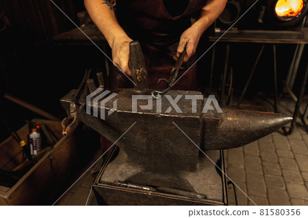 Close-up working powerful hands of male blacksmith forge an iron product in a blacksmith. Hammer, red hot metal and anvil. Concept of labor, retro professions Close-up working powerful hands of male blacksmith forge an iron product in a blacksmith. Hammer, red hot metal and anvil. Concept of labor, retro professions 81580356