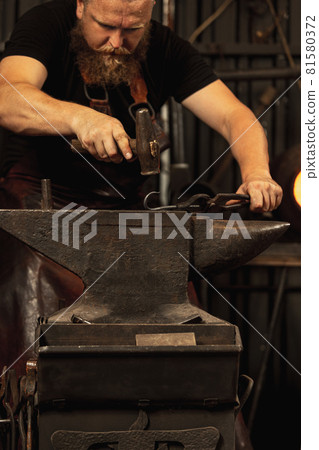 Bearded man, blacksmith working on creating handmade metal product at family smithy. Concept of labor, retro professions, power, beauty Bearded man, blacksmith working on creating handmade metal product at family smithy. Concept of labor, retro professions, power, beauty 81580372