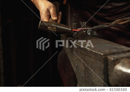 Close-up working powerful hands of male blacksmith forge an iron product in a blacksmith. Hammer, red hot metal and anvil. Concept of labor, retro professions 81580380