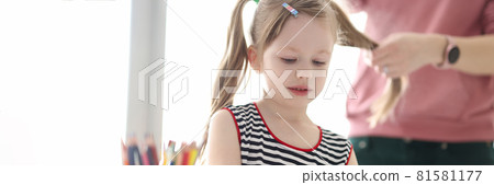 Little girl drawing with pencils. Mother braiding child hair Little girl drawing with pencils. Mother braiding child hair 81581177