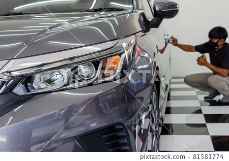 Details of the car. A male mechanic is applying a glass-ceramic coating on the car at the shop. 81581774