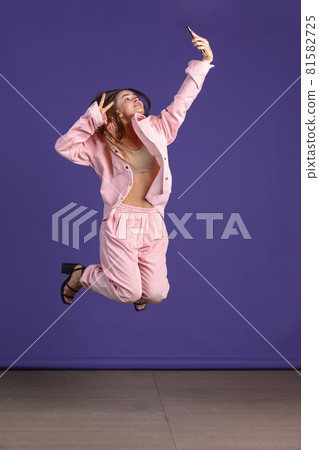 Full-length portrait of young attractive girl jumping over purple studio background Full-length portrait of young attractive girl jumping over purple studio background 81582725