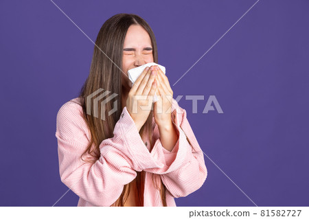 Cropped portrait of young beautiful woman sneezing on purple background Cropped portrait of young beautiful woman sneezing on purple background 81582727