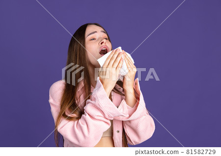 Cropped portrait of young beautiful woman sneezing on purple background Cropped portrait of young beautiful woman sneezing on purple background 81582729