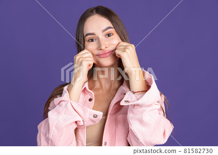 Cropped close-up portrai of young beautiful woman making funny faces on camera isolated over purple background Cropped close-up portrai of young beautiful woman making funny faces on camera isolated over purple background 81582730