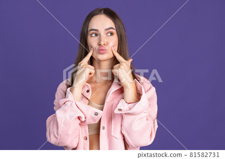 Close-up portrait of young beautiful girl making faces on purple studio background Close-up portrait of young beautiful girl making faces on purple studio background 81582731