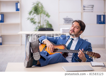 Young male employee playing guitar at workplace Young male employee playing guitar at workplace 81583123